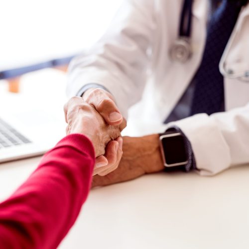 Male doctor with laptop and a senior woman in his office, shaking hands.