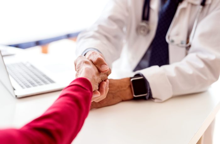 Male doctor with laptop and a senior woman in his office, shaking hands.